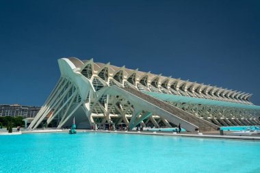 Valencia, İspanya - 12 Ağustos 2022: Prncipe Felipe Bilim Müzesi 'nin açık mavi gökyüzü altında yansıtıcı turkuaz havuzunun üzerinde süzülen beyaz kurdeleli perdesi.