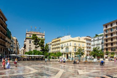 Valencia, İspanya - 12 Ağustos 2022: Turistler Plaza de la Virgen 'deki Turia Çeşmesi' nin yanında açık kafeleri ve Valenciana Generalitat binası ile berrak bir gökyüzü altında yürüyüp dinleniyorlar.