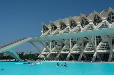 Valencia, İspanya, 12 Ağustos 2022: Bir aile, Prncipe Felipe Bilim Müzesi 'nin çarpıcı beyaz tırtıklı cephesinin önündeki turkuaz yansıma havuzunda kürek çekiyor..