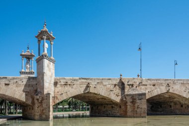 Pont del Mar taş köprüsü ve bakire heykeli Turia Gardens su kanalının üzerinde durmakta açık mavi gökyüzünün altında.