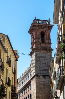 Serranos Kulesi 'nin üst tuğla ve taş seviyelerinin yakın çekimi açık mavi gökyüzünün altında dar yerleşim alanları arasında yükseliyor.