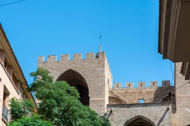 Ortaçağ Serranos Kulelerinin arka manzarası yemyeşil sokak ağaçlarının üzerinde yükseliyor ve taş kemerlerinin altında yürüyen ziyaretçiler.