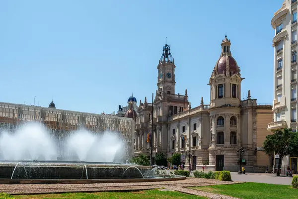Valencia, İspanya - 12 Ağustos 2022: Süslü macenta kaplı belediye binası, hareketli Plaza del Ayuntamiento Meydanı 'ndaki dairesel bir fıskiyenin çağlayan su fıskiyeleri tarafından çerçevelenmiştir..