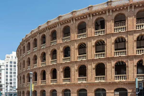 Valencia, İspanya - 12 Ağustos 2022 Plaza de Toros de Valencia 'nın kıvrımlı tuğla kemerlerinin yanından geçen yayalar, açık mavi gökyüzünün altındaki 19. yüzyıldan kalma bir bulvar taşı..