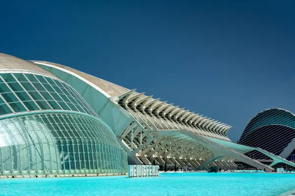 Valencia, İspanya - 12 Ağustos 2022: Sanat ve Bilim Şehri 'nde Hemisferic' in yan perspektifi, cam kubbesi, iskelet kemerleri ve havuzu yansıtan turkuaz.
