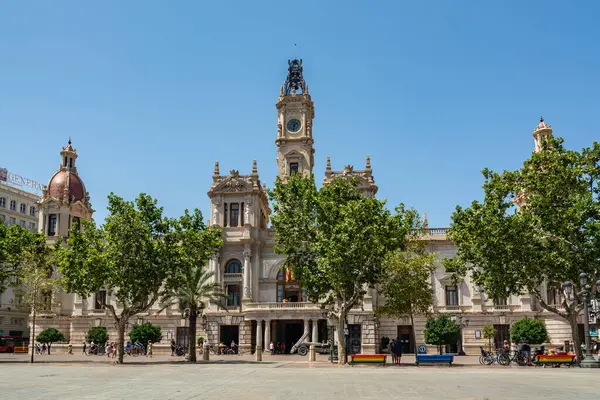 Valencia, İspanya - 12 Ağustos 2022: Ağaç kaplı Plaza del Ayuntamiento Valensiya Belediye Binası 'nın süslemeli neoklasik ön cephesini ve saat kulesini çerçeveler..