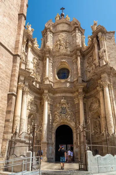 Valencia, İspanya - 12 Ağustos 2022: Ziyaretçiler, Valencia Katedrali 'nin zengin oyulmuş Barok kapısından Korint sütunları ve açık bir gökyüzünün altındaki yardım heykellerinden içeri girerler.