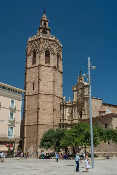 Valencia, İspanya - 12 Ağustos 2022: Ziyaretçiler, yükselen çan kulesine ve GothicBaroque taş cephelerine hayran kalarak Valencia Katedrali 'nin dışındaki güneşli bir plazada geziniyorlar..
