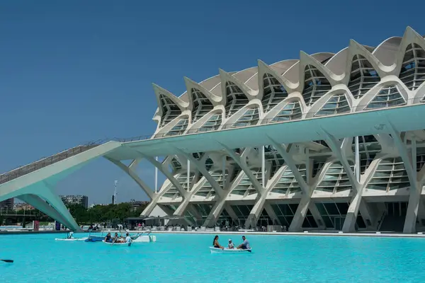 Valencia, İspanya, 12 Ağustos 2022: Bir aile, Prncipe Felipe Bilim Müzesi 'nin çarpıcı beyaz tırtıklı cephesinin önündeki turkuaz yansıma havuzunda kürek çekiyor..