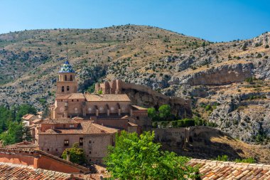 Döşemeli katedral kulesi terracotta çatıları ve berrak mavi gökyüzünün altındaki engebeli kireçtaşı kayalıklarıyla çerçevelenmiştir..