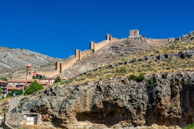 Katedralin fayanslı kulesi, açık mavi gökyüzünün altında, terracotta binalarının ve engebeli uçurumların üzerinde yükselir..