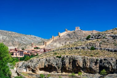 Katedralin fayanslı kulesi, açık mavi gökyüzünün altında, terracotta binalarının ve engebeli uçurumların üzerinde yükselir..