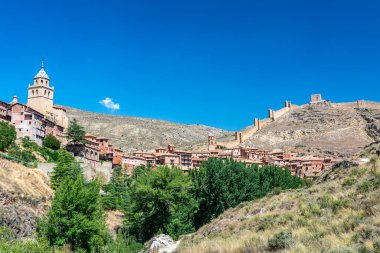 Katedralin fayanslı kulesi, açık mavi gökyüzünün altında, terracotta binalarının ve engebeli uçurumların üzerinde yükselir..