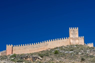 Ortaçağ kalesinin çentikli taş duvarlarının ve derin bir kobalt gökyüzünün altındaki kayalık sırtta yükselen kulesinin fotoğrafı..