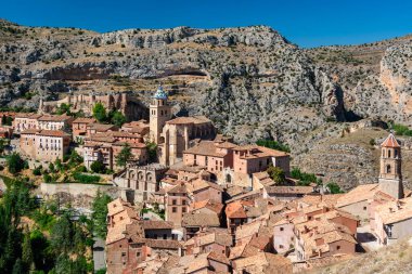 Sarmal kırmızı çatılı ortaçağ evlerinin, taş duvarların ve engebeli tepelere kurulmuş kilise kulesinin panoramik görüntüsü..
