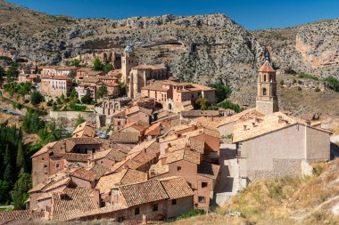 Sarmal kırmızı çatılı ortaçağ evlerinin, taş duvarların ve engebeli tepelere kurulmuş kilise kulesinin panoramik görüntüsü..