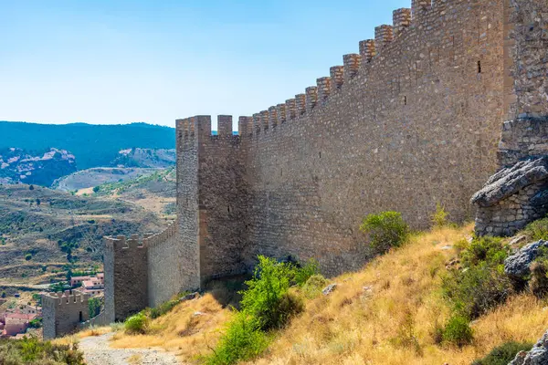 Çırpılmış ortaçağ kale duvarının geniş açılı görüntüsü tarihi Albarracin kasabasının üstündeki kayalık yamaçtan aşağı sarkıyor..