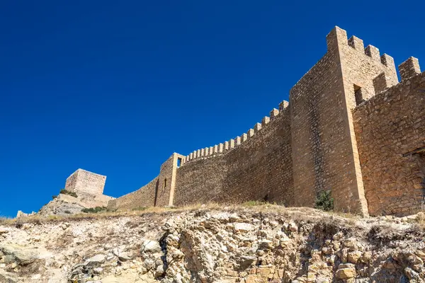 Çırpılmış ortaçağ kale duvarının alçak açılı görüntüsü kayalık yamaçta, açık bir kobalt gökyüzünün altında..