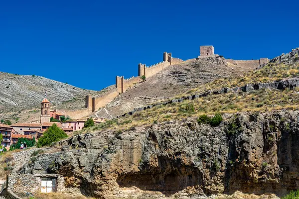 Katedralin fayanslı kulesi, açık mavi gökyüzünün altında, terracotta binalarının ve engebeli uçurumların üzerinde yükselir..