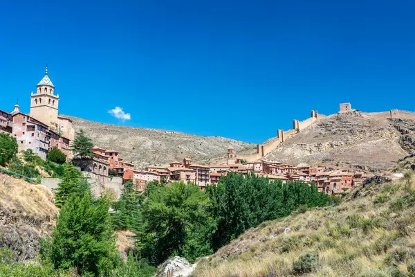 Katedralin fayanslı kulesi, açık mavi gökyüzünün altında, terracotta binalarının ve engebeli uçurumların üzerinde yükselir..