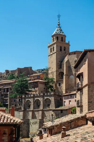 Katedralin fayanslı kulesi, açık mavi gökyüzünün altında, terracotta binalarının ve engebeli uçurumların üzerinde yükselir..