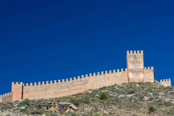 Ortaçağ kalesinin çentikli taş duvarlarının ve derin bir kobalt gökyüzünün altındaki kayalık sırtta yükselen kulesinin fotoğrafı..