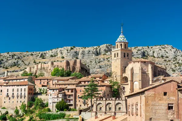 Katedralin fayanslı kulesi, açık mavi gökyüzünün altında, terracotta binalarının ve engebeli uçurumların üzerinde yükselir..