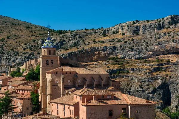 Katedralin fayanslı kulesi, açık mavi gökyüzünün altında, terracotta binalarının ve engebeli uçurumların üzerinde yükselir..