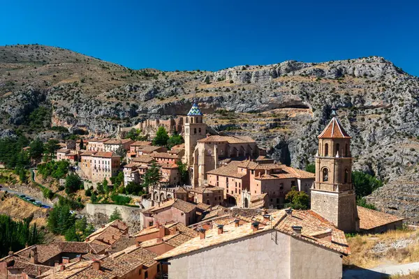 Sarmal kırmızı çatılı ortaçağ evlerinin, taş duvarların ve engebeli tepelere kurulmuş kilise kulesinin panoramik görüntüsü..