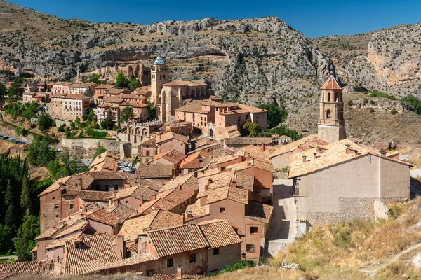 Sarmal kırmızı çatılı ortaçağ evlerinin, taş duvarların ve engebeli tepelere kurulmuş kilise kulesinin panoramik görüntüsü..