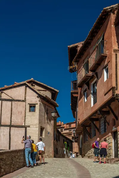 Albarakin, İspanya - 15 Ağustos 2022: Ziyaretçiler, güneşli bir ortaçağ caddesi boyunca kereste çerçeveli ve terasotta cepheli, dik kaldırım taşı patikalı gezintiler ve fotoğraflar çekiyorlar.