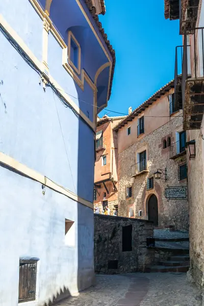 Albarakin, İspanya - 15 Ağustos 2022: Pastel mavi cepheli ve kırsal taş binalı günışığı ortaçağ sokağı, balkonlar ve kemerli pencerelerle çevrili dar kaldırım taşı yolu.