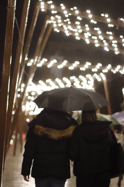 İnsanlar Noel zamanı yağmurlu bir kış gecesinde San Sebastian 'da köprüden geçiyorlar.
