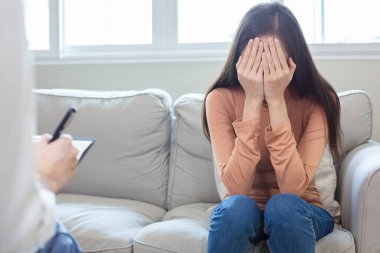 Kanepede oturan ve yüzünü kapatan depresyonlu elleri olan bir kadın. Hastalığını tedavi etmek için psikiyatristle tanış. Hasta depresyonu kadın terapisi tedavisi.