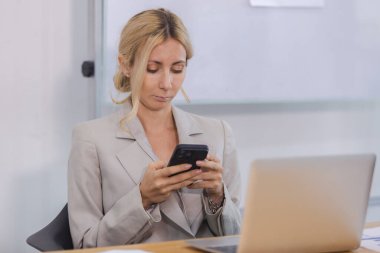 Ofiste oturan cep telefonu kullanan bir iş kadını. Bayan sohbetçi mesaj yazıyor. Ofiste akıllı telefonda..