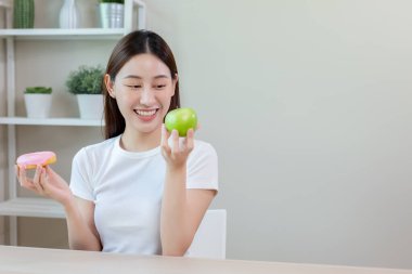 Beautiful asian female smiling holding apple and donut choosing healthy eat. healthy food choices. Girl keep their diet. Diet healthy food concept.