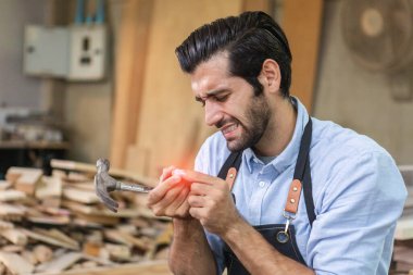 young carpenter man worker in wood factory accident hammer bump finger. have pain a finger.