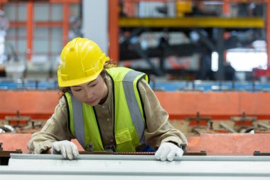 Asian female workers wear red helmet working check up iron production in factory. woman in heavy Industrial manufacturing workplace.