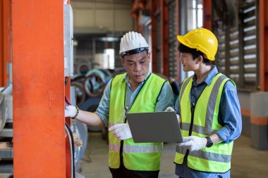 İki endüstri mühendisi, ağır sanayi imalatındaki fabrikaların dizüstü bilgisayar öğrenme projesini kullanarak sabit şapka ve üniforma giyer. Denetçi çalışana öğretmenlik yapıyor..