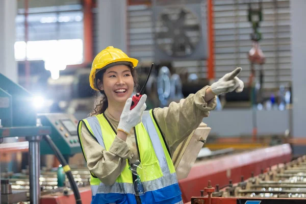 Mutlu gülümseyen kadın mühendis elinde telsiz ile parmağını ileri doğru uzat ve fabrika deposunun önünde dur. profesyonel mühendislik makine atölyesi.