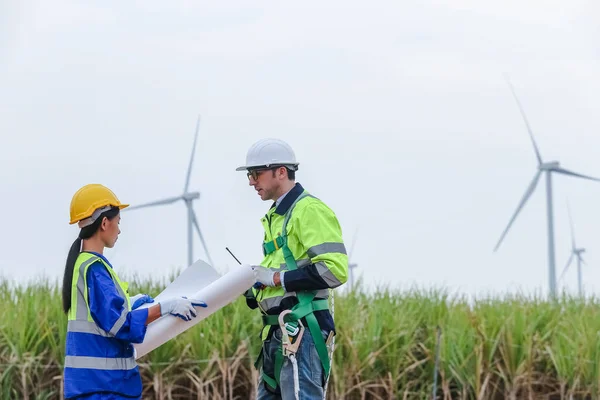 Team engineer of wind turbine worker pointing holding blueprint working about renewable energy at station energy power wind. technology protect environment reduce global warming problems.