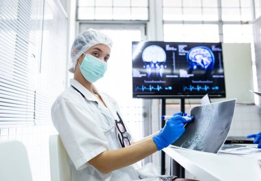 Genç bayan sağlık görevlileri maske ve mavi eldivendi. Kalemi al ve röntgen filmine doğrult. Beyin cerrahisini öğren. Tıp öğrencileri X-ray filmlerinden öğrenerek beyin hastalıkları teşhisi koyuyorlar..