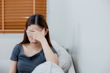 Kanepede yalnız oturan depresyonda bir kadın. Yüzü baş ağrısıyla kaplı bir kadın. Mutsuz duygu. gençlik umutsuzluğu zihinsel sağlık sorunları.