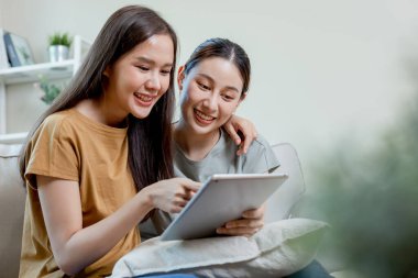 Mutlu kadın çift evdeki kanepede otururken dijital tablet alışverişi yapıyor. Güzel kadın kız arkadaş yaşam tarzı. İnternette film izleyen iki kız..