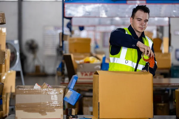 仓库包装纸板箱产品用包装带包装安全制服的金发男工 — 图库照片