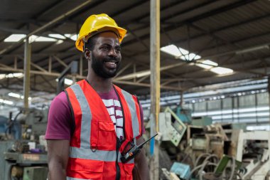 Portre mühendisliği erkek Afro-Amerikan mutlu gülümseyen işçiler fabrika sanayisinde ayakta duran sarı, kırmızı şapka giyiyorlar. Erkek teknisyen makine uzmanı iş yerinde.