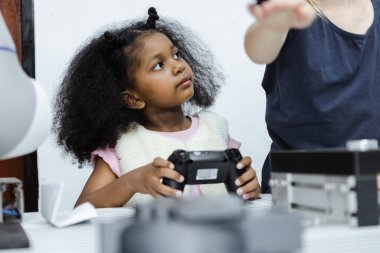 Çocuklar, Afrika kökenli Amerikalı kız, sınıftaki masada joystick eğitimi için elektronik aletler tutuyor. Gelecekteki yapay zekalar için elektronik öğrenme teknolojisi. Elektrik sistemi eğitimi. BTMM eğitim kavramı.