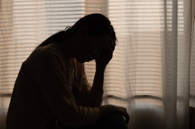 Yatak odasının karanlık köşesinde depresyonda olan bir kadın. Kadın baş ağrısı, mutsuz duygu. Depresyonda olan genç zihinsel sağlık sorunları. Koyu Ton.