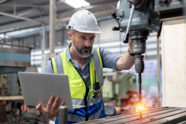 Kafkasyalı mühendis, ağır sanayi fabrikasında çalışırken beyaz şapka takar ve güvenlik üniforması giyer. Erkek çalışma makinesi metal torna..