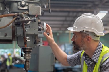 Kafkasyalı mühendis beyaz şapka takıyor ve çelik matkap fabrikasında çalışan güvenlik üniforması giyiyor. Erkek çalışma makinesi metal torna..